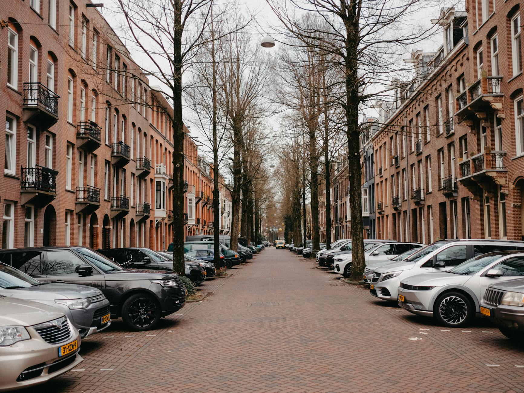 Cicha ulica w Amsterdamie z ceglanymi kamienicami i zaparkowanymi samochodami