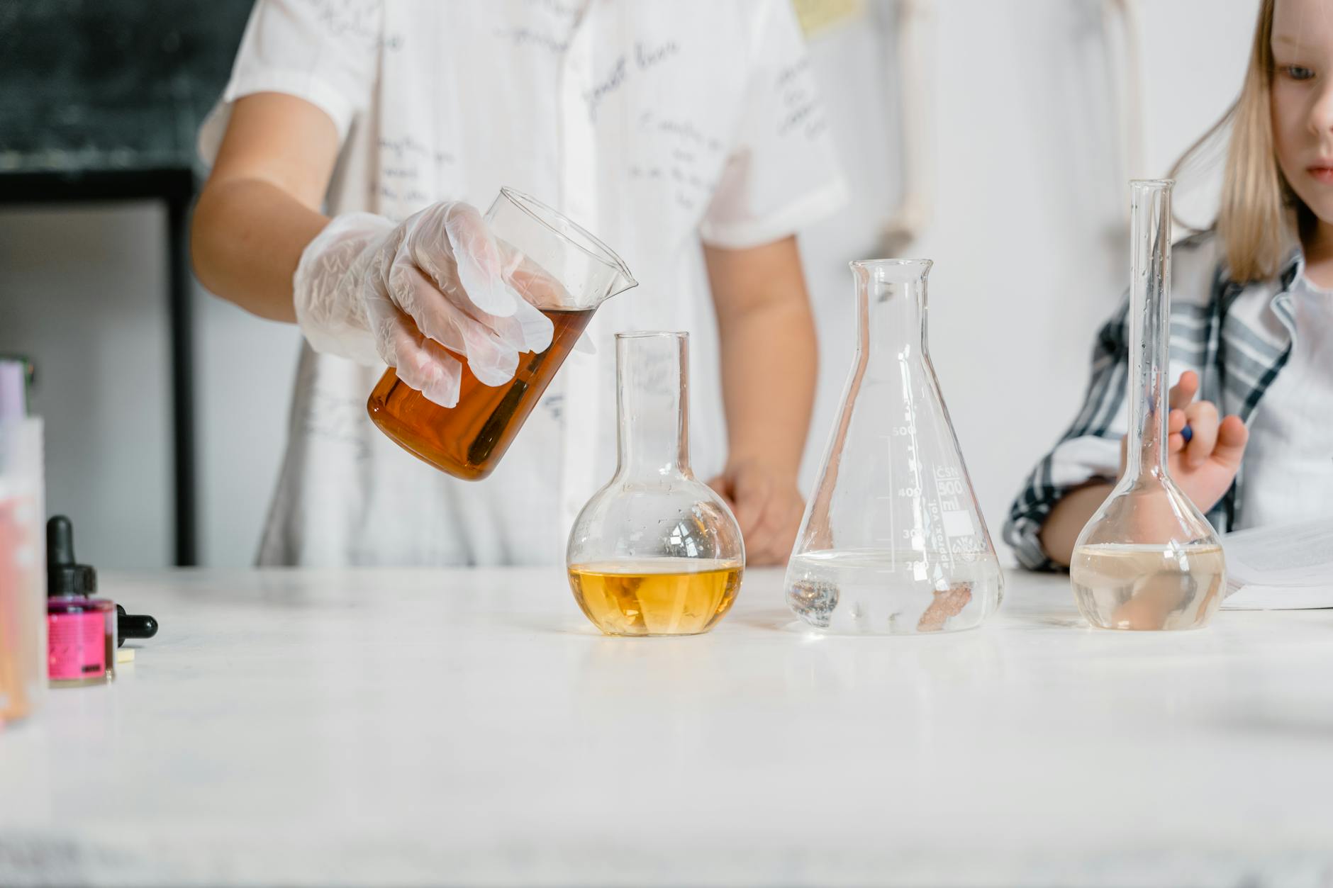 Uczniowie wykonują doświadczenie chemiczne z kolbami i kolorowymi roztworami Uczniowie wykonują doświadczenie chemiczne z kolbami i kolorowymi roztworami