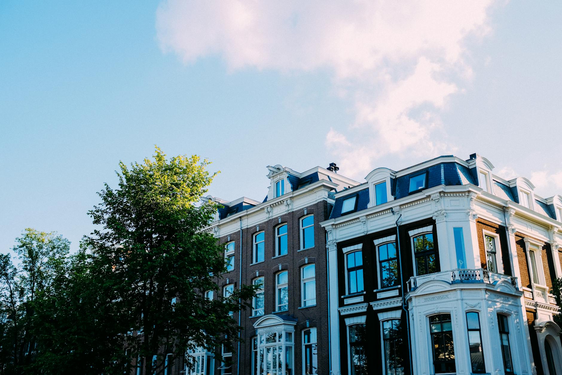 Amsterdam jak mieszkaniec: dzielnice, w których turysta rzadko bywa Zabytkowa kamienica w Amsterdamie za zielonymi drzewami w słoneczny dzień